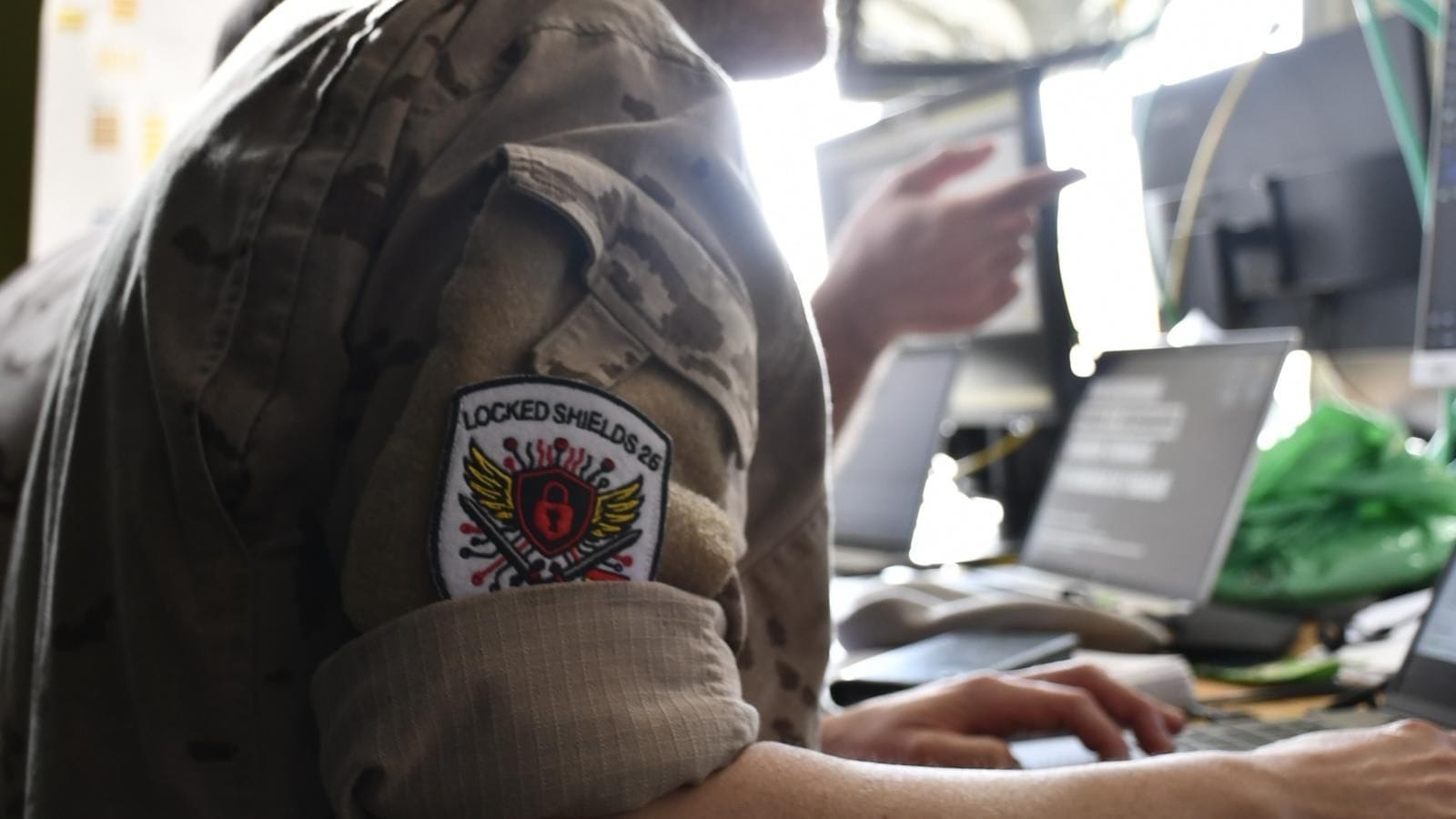Military operator wearing a Locked Shields 26 patch working on cyber defense systems during the NATO live-fire exercise.